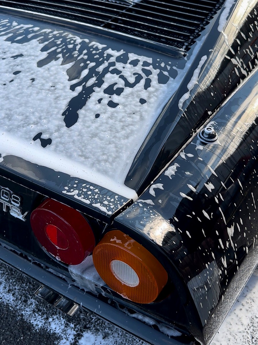 Mousse de lavage ruisselant sur la carrosserie noire d’une voiture de collection — photographie réelle
