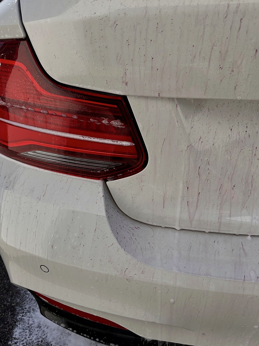 Coulures violettes d’un produit de décontamination sur le feu arrière et le pare-chocs d’une carrosserie blanche — photographie réelle